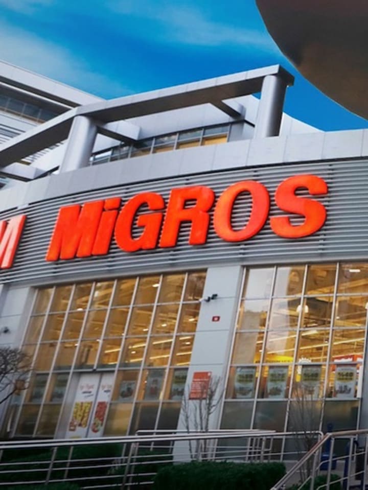 Migros mağazasının cam cepheli girişi ve aydınlatmalı tabelası